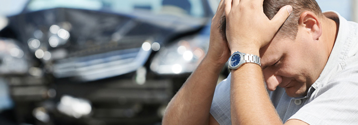 Person sitting with head in hands in front of a damaged car after an accident