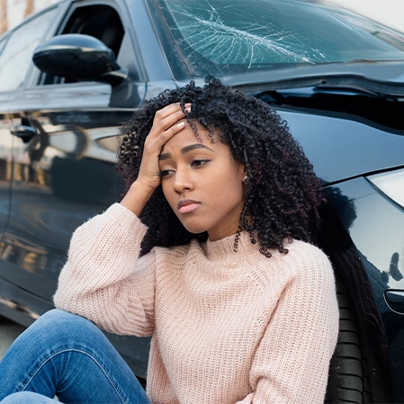 Person sitting on the ground near a damaged black car