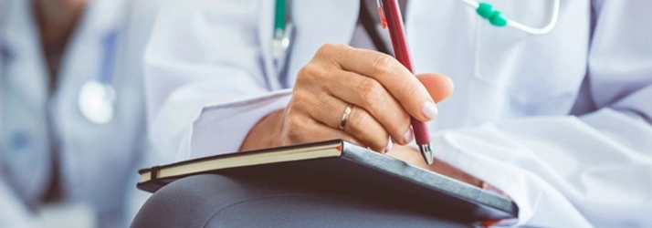 Doctor in a white coat writing notes in a notebook with a pen