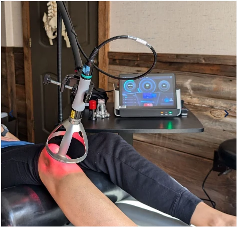 A therapeutic device emitting red light is positioned over a person’s knee 