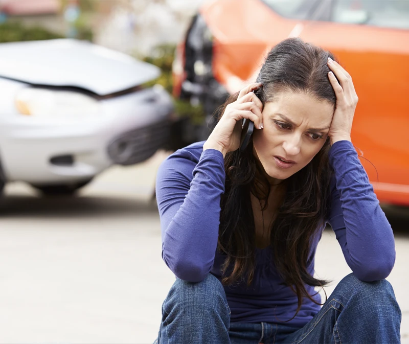 A person holding a phone to their head with the crash‑damaged vehicles visible behind them